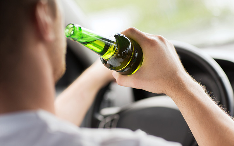 Mann trinkt Bier beim Autofahren