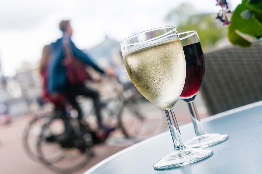 Zwei Weingläser auf einem Tisch und im HIntergrund zwei Fahrradfahrer