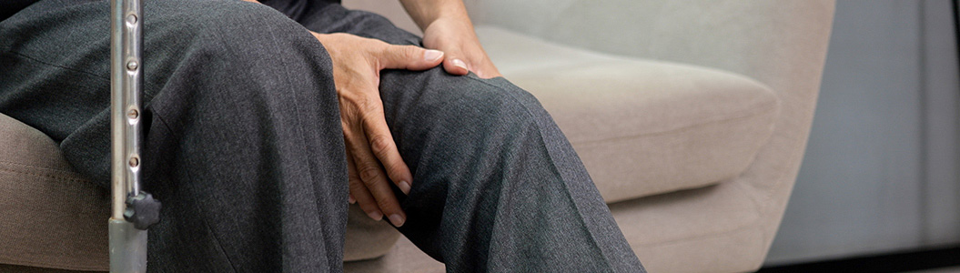 Senior grandfather with walking stick trying to exercise knee and leg on sofa at home, Elderly man with knee joint pain and suffering